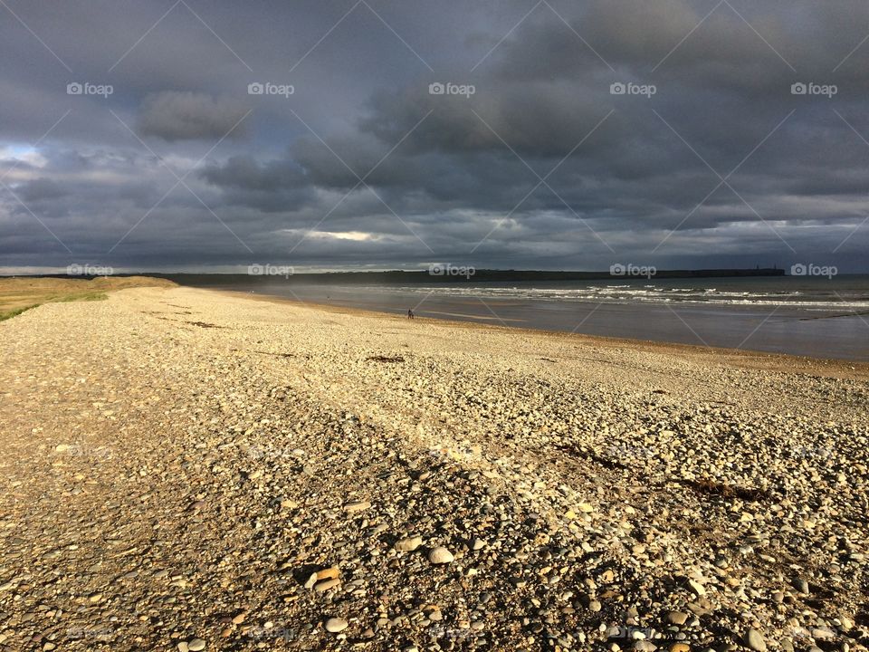 Sunlit shingle beach with dark, cloudy sky
