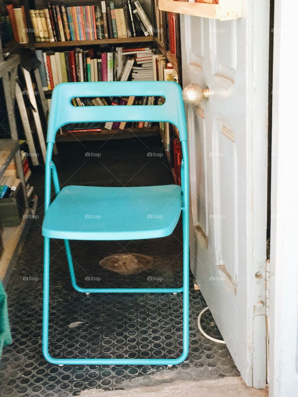 Turquoise simple chair standing in the doorway into a book store 