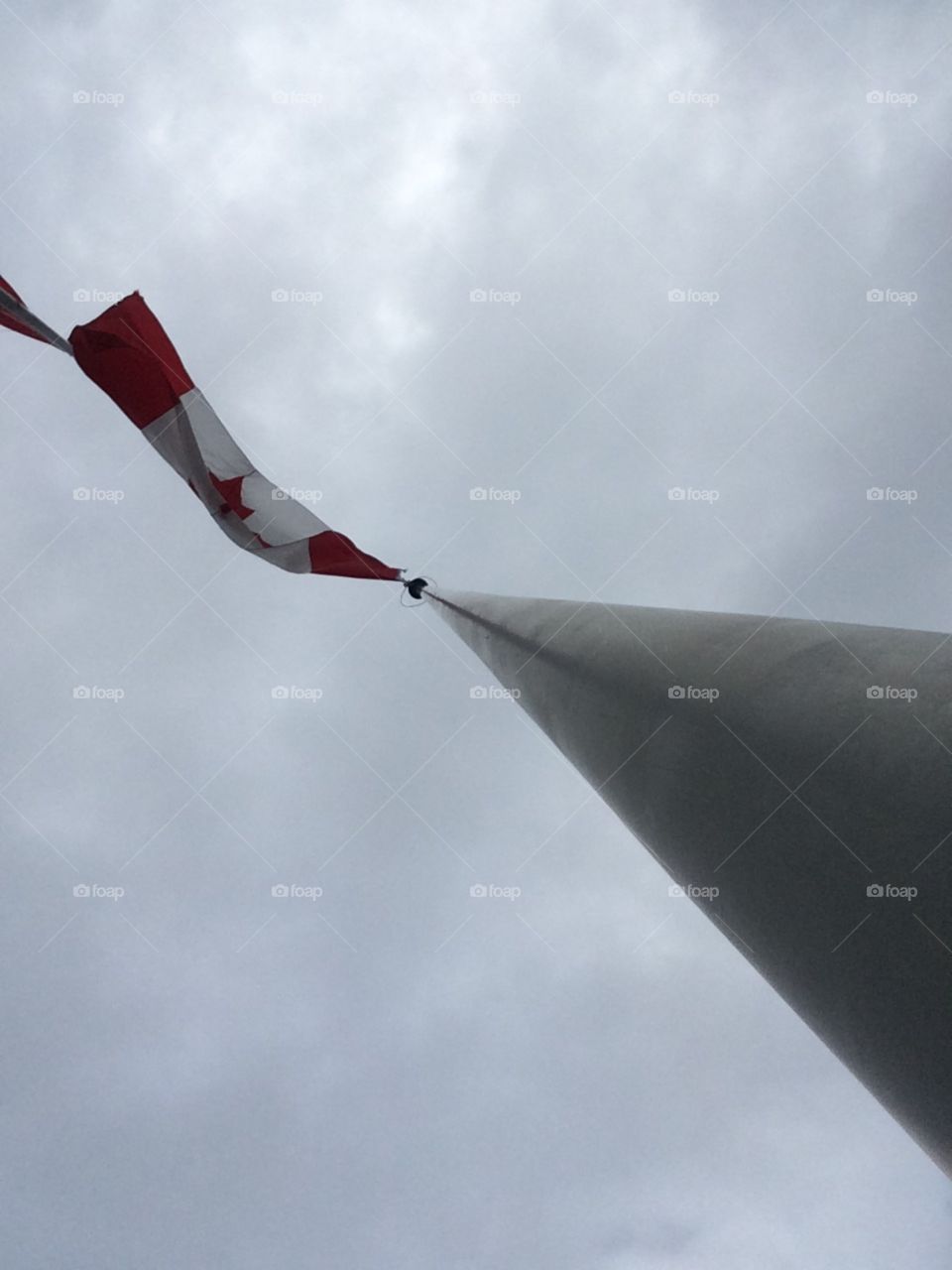 Beautifully angled photo of a red and white flag, also known as the Canadian flag. A dark cloud covered sky is featured up above