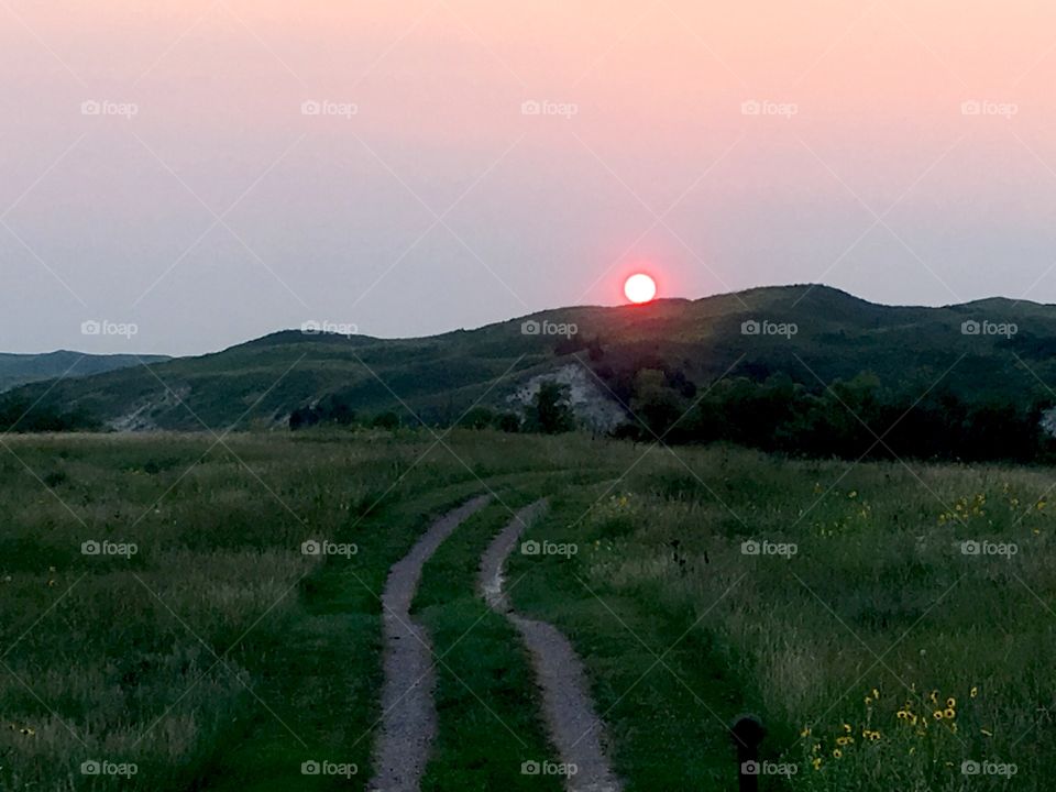 Sand trail through the Nebraska sand hills with the orange sun setting behind s hill. 