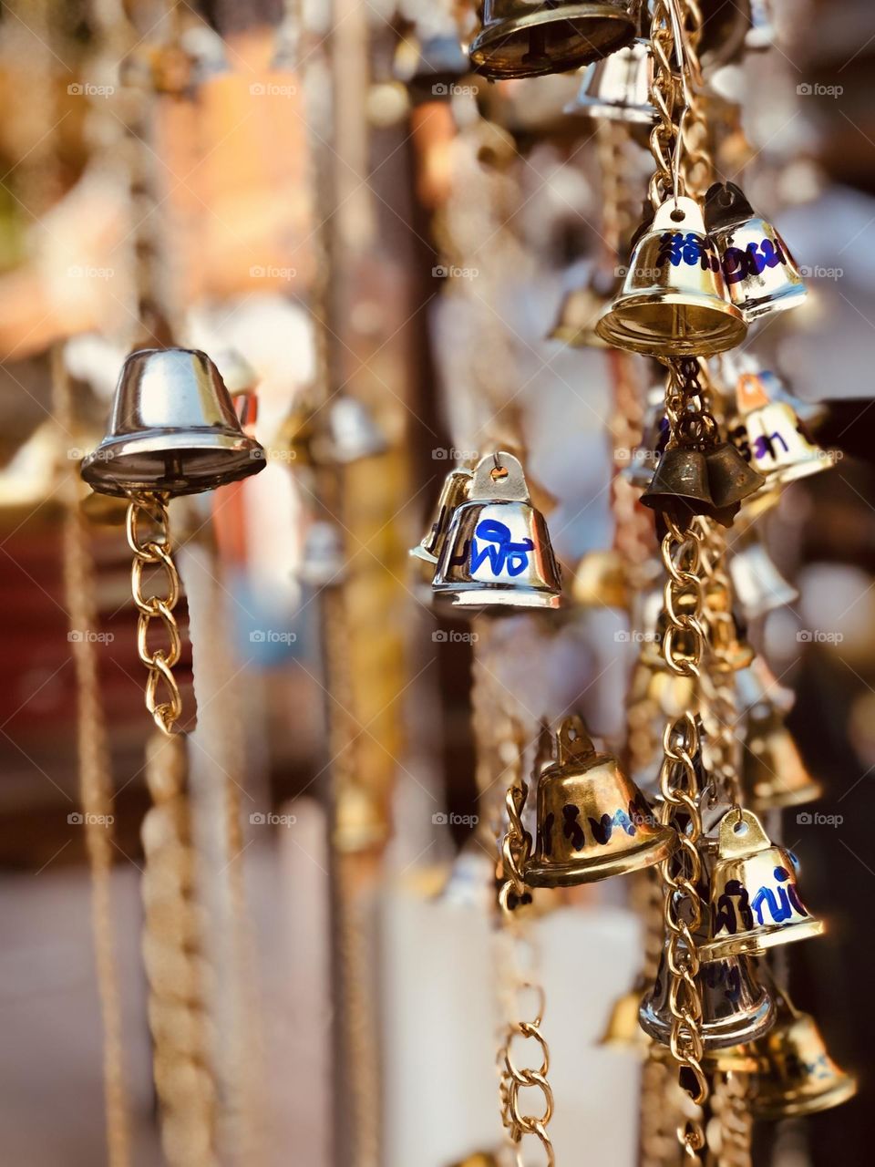 Golden metal votive bells at the entrance of a temple hanged with chains 