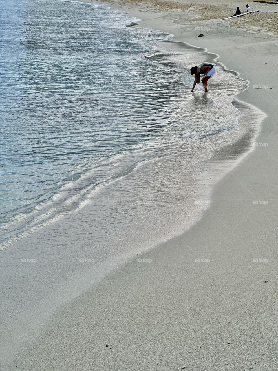 An early morning beach goer rinses off her sandal and two local surfers sit and wait for the tide to come back in in Hawaii