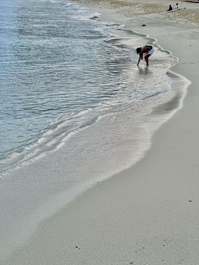 An early morning beach goer rinses off her sandal and two local surfers sit and wait for the tide to come back in in Hawaii
