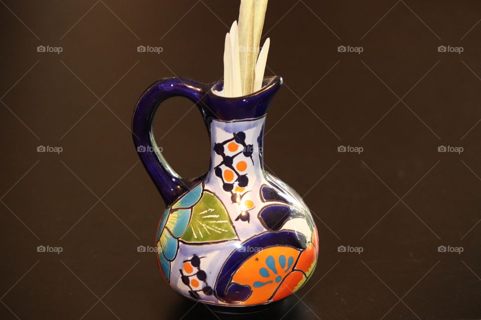 Colorful Amphora vase with bird feathers inside against dark background 