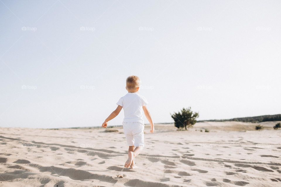 Small boy in white clothes running on desert