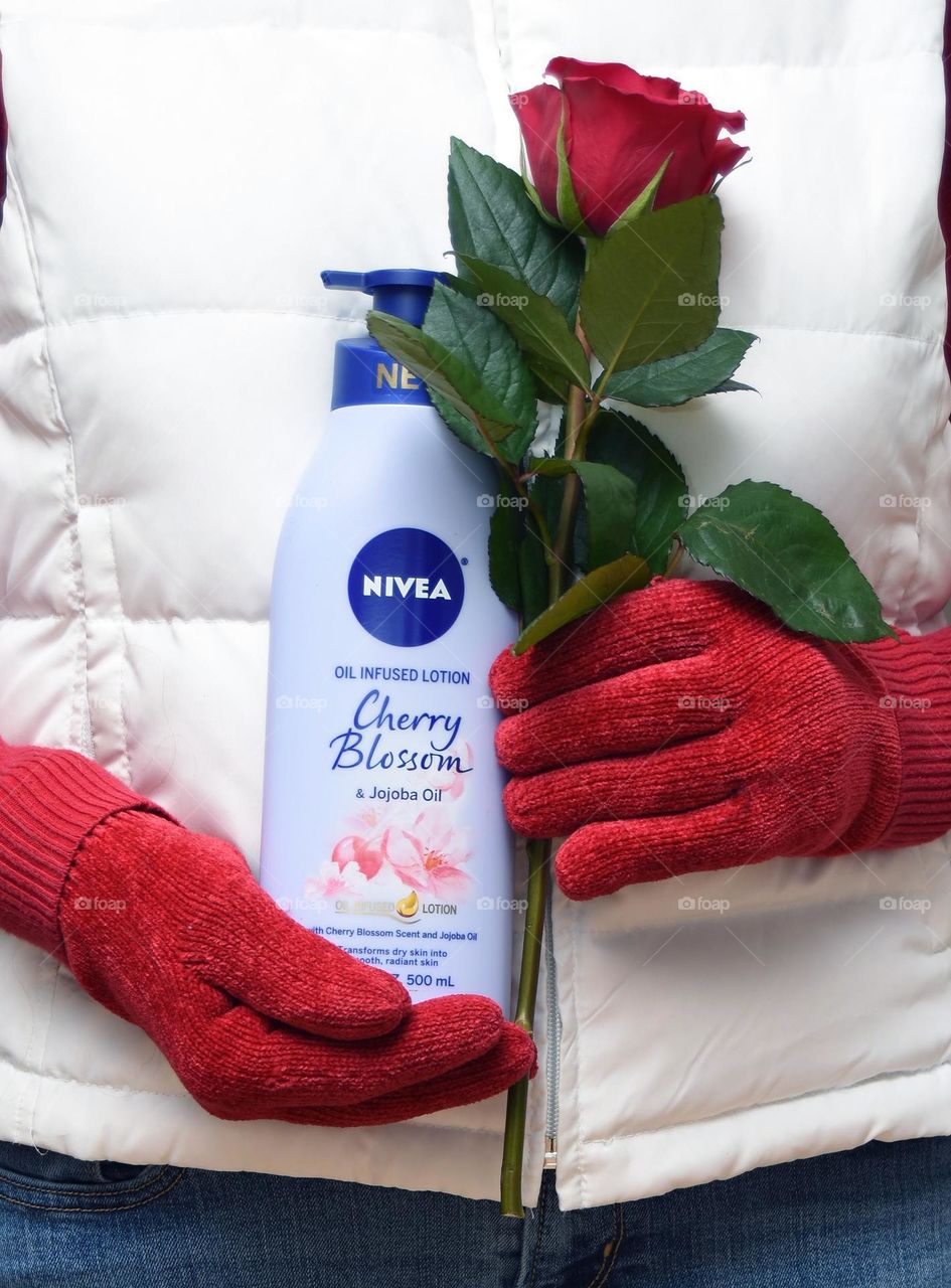 Nivea beauty product held by hands in red gloves holding a red rose, wearing a white vest 