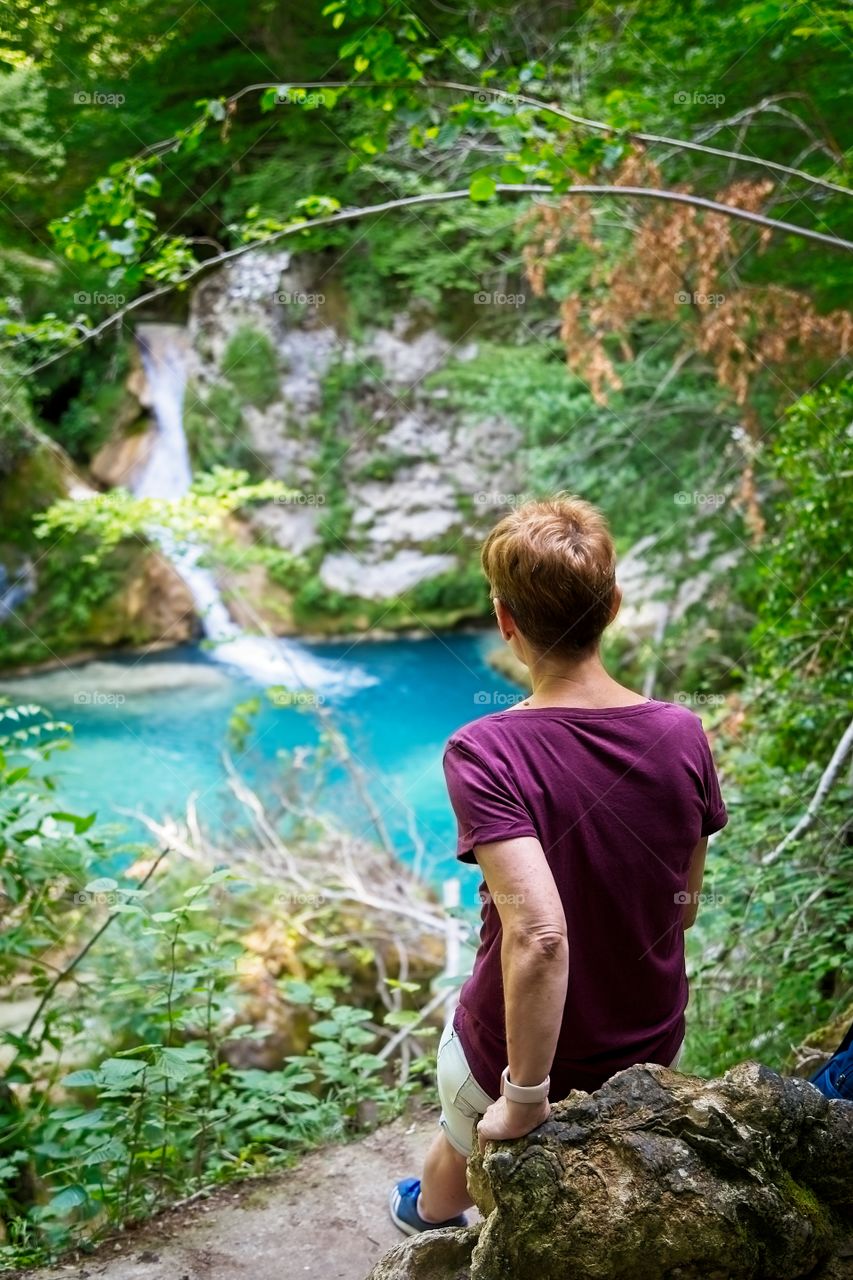 A woman contemplates a waterfall and a beautiful blue lake 