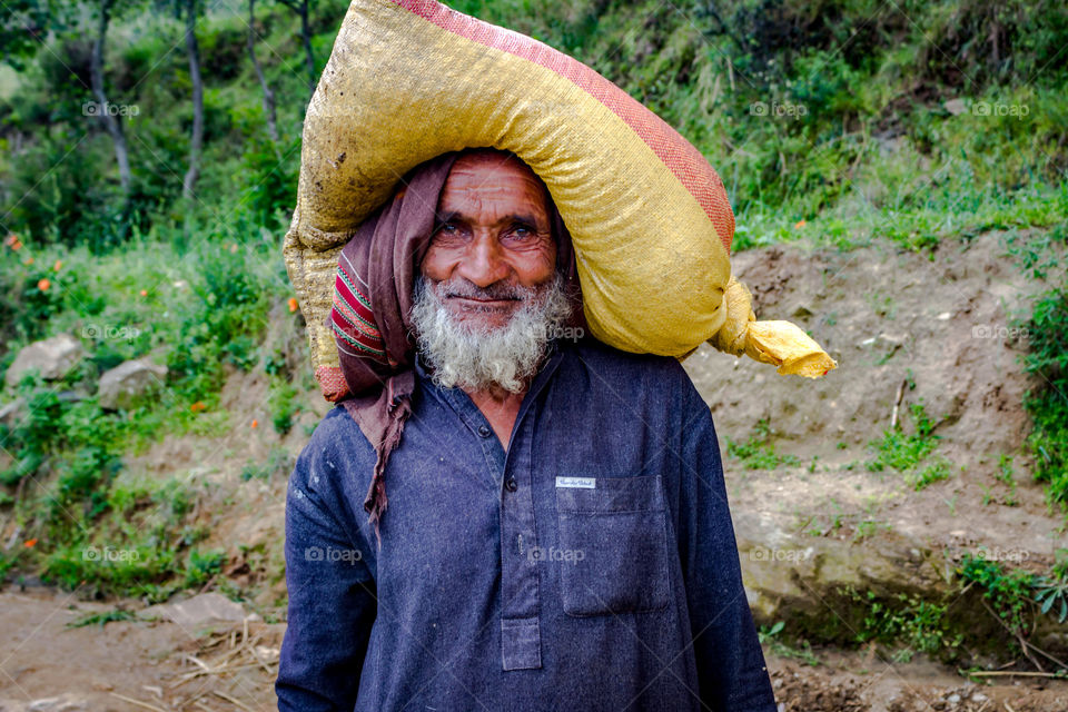 Portrait of a senior man carrying sack on head