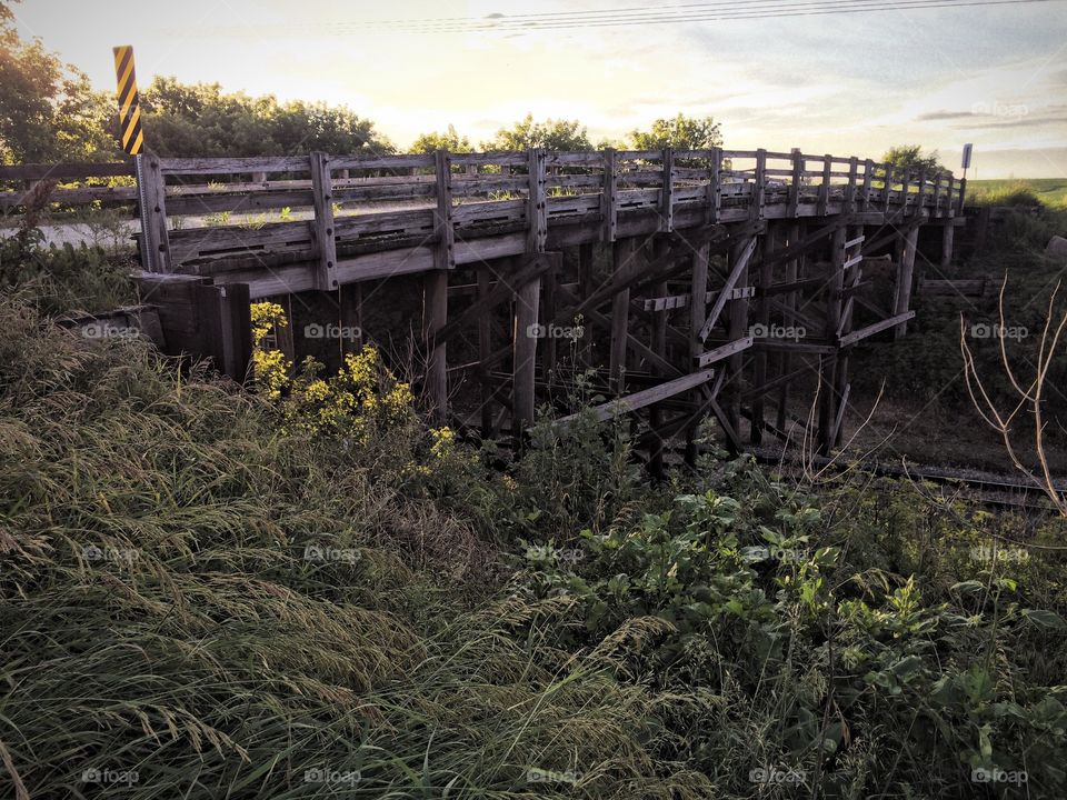 Old wooden bridge carrying rural gravel road over railroad tracks in Iowa. 