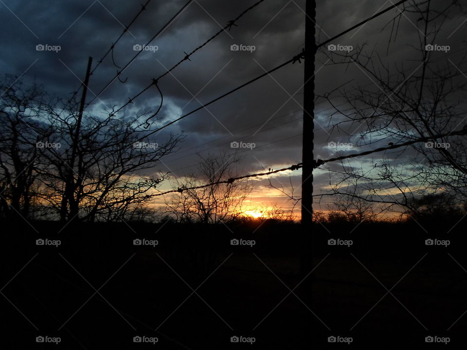 sunrise on a cloudy morning through the farm fence