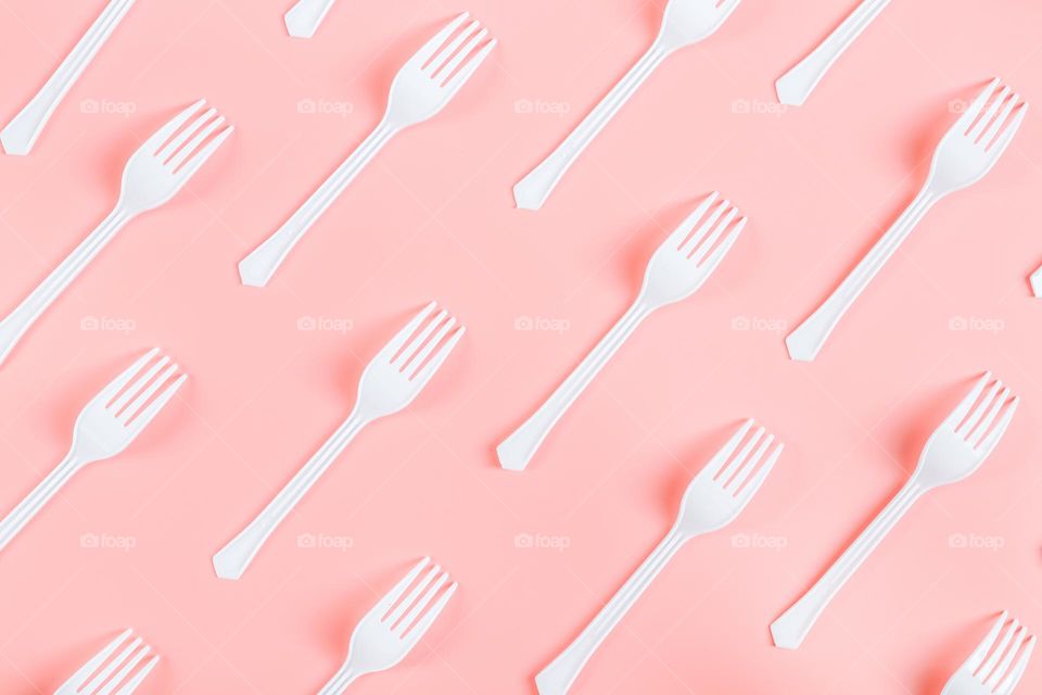 A lot of white plastic forks lying diagonally on a pink background, flat lay close-up. Cutlery and ecology concept.