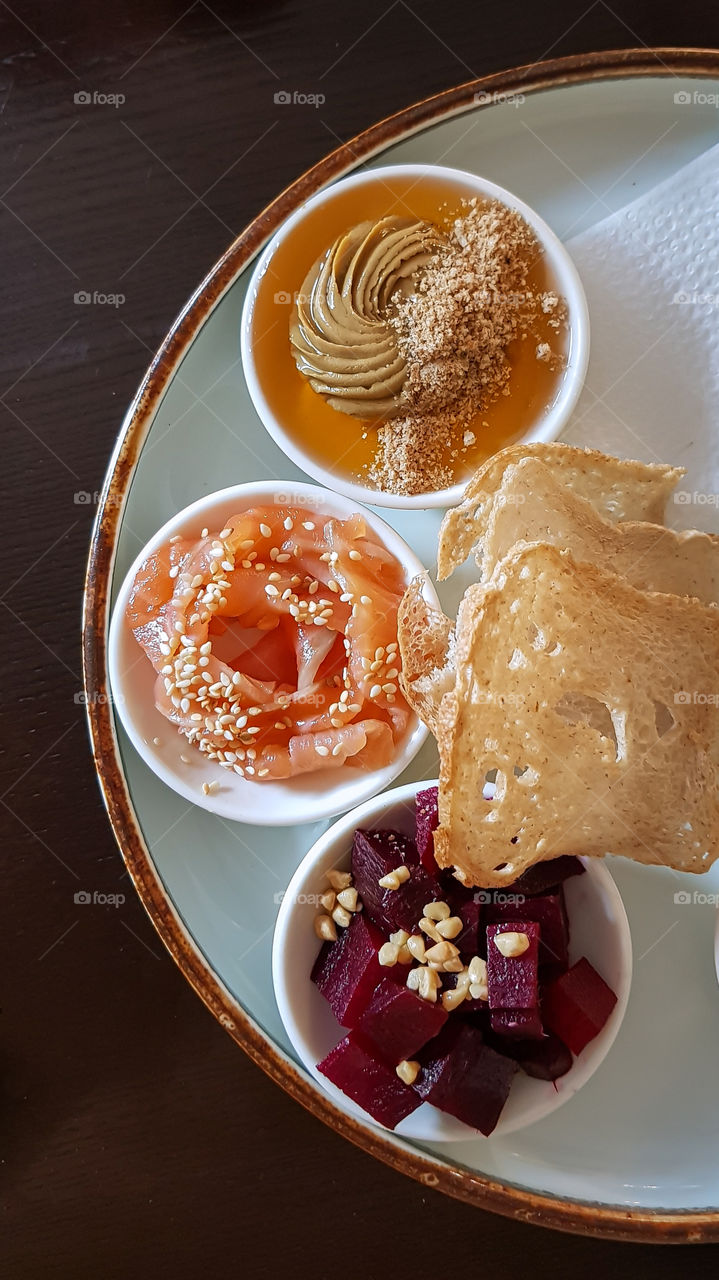 Bowls with a selection of healthy snacks such as confit pate, red beets with chopped nuts, salmon wedges with sesame seeds, and yeast-free bread chips.