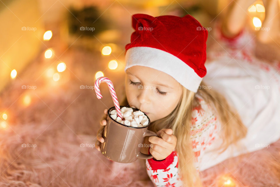 Cute little girl in Christmas pajamas drinking hot cacao at home