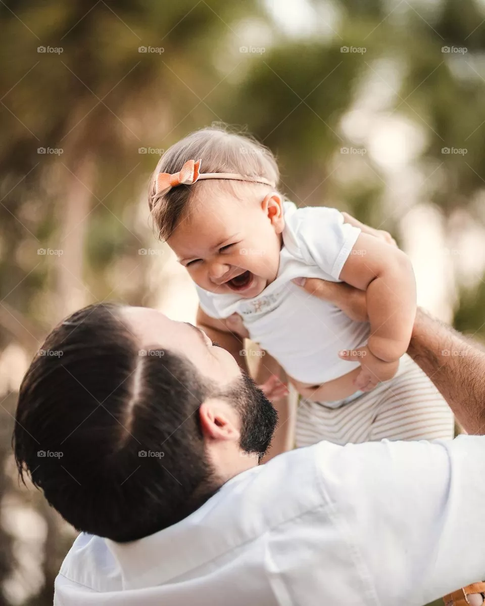 Gorgeous color photo of a father holding up his daughter, making her smile in a beautifully captured moment. Fall and autumn colors make way for a warm feeling of this cuddly couple.