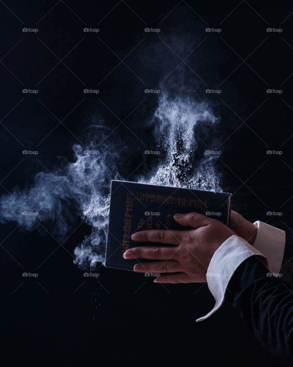the end of an era close the book this image shows a pair of hands closing a book with dust spraying out as the book closes. black sleeves white trim dark blue book cover with powder actively blowing out as the book closes against black background
