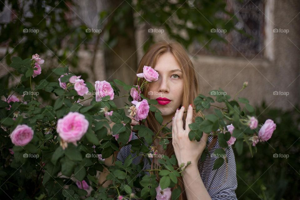 Beautiful girl with the bush of blooming roses 