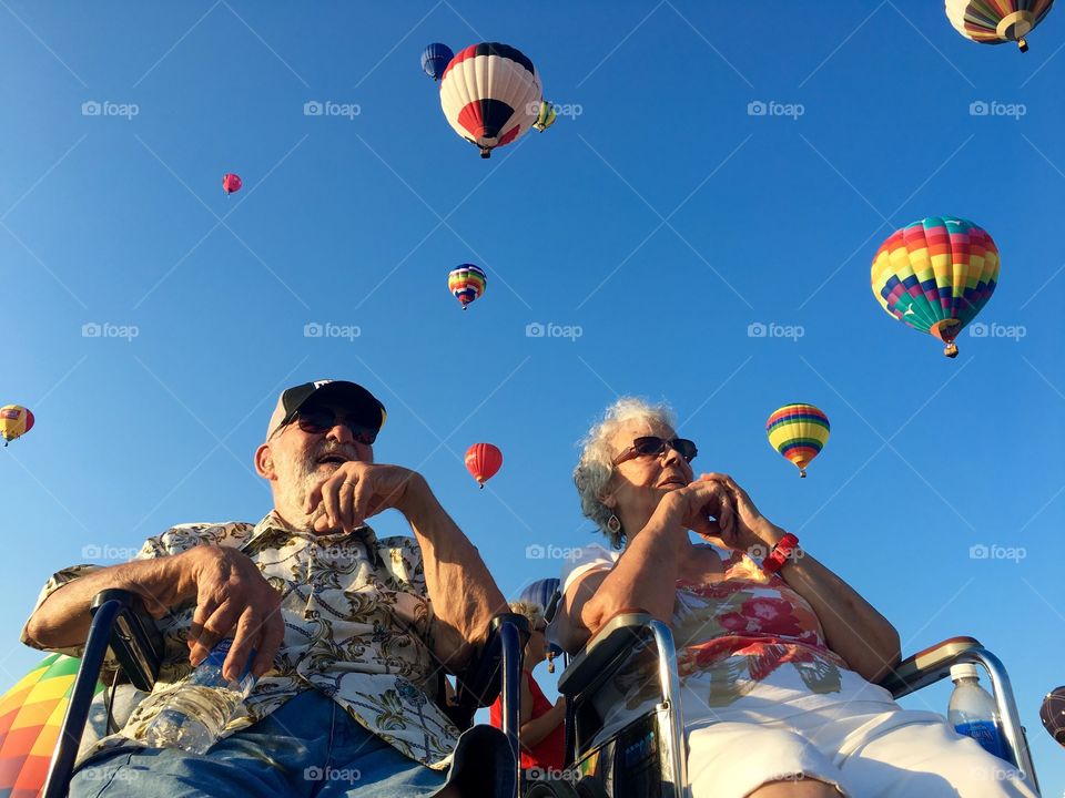 Senior couple sitting against hot air balloons in sky