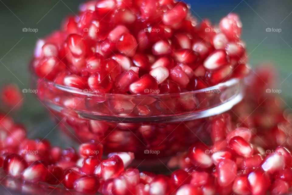 Fruits! - Closeup of fresh pomegranate seeds overflowing a small glass bowl against a green background