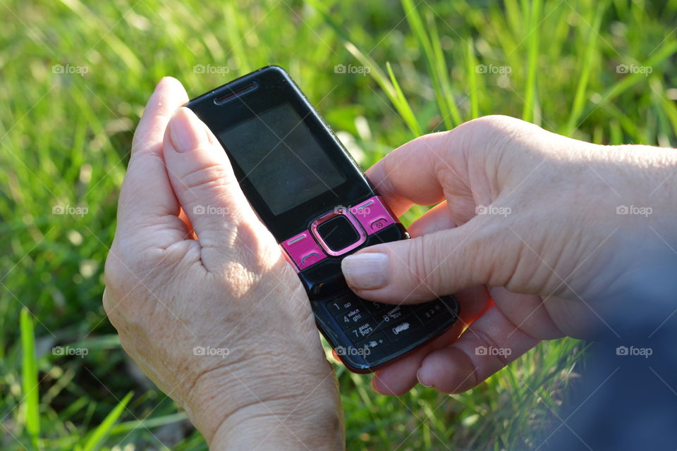 old phone in the female hands green summer background