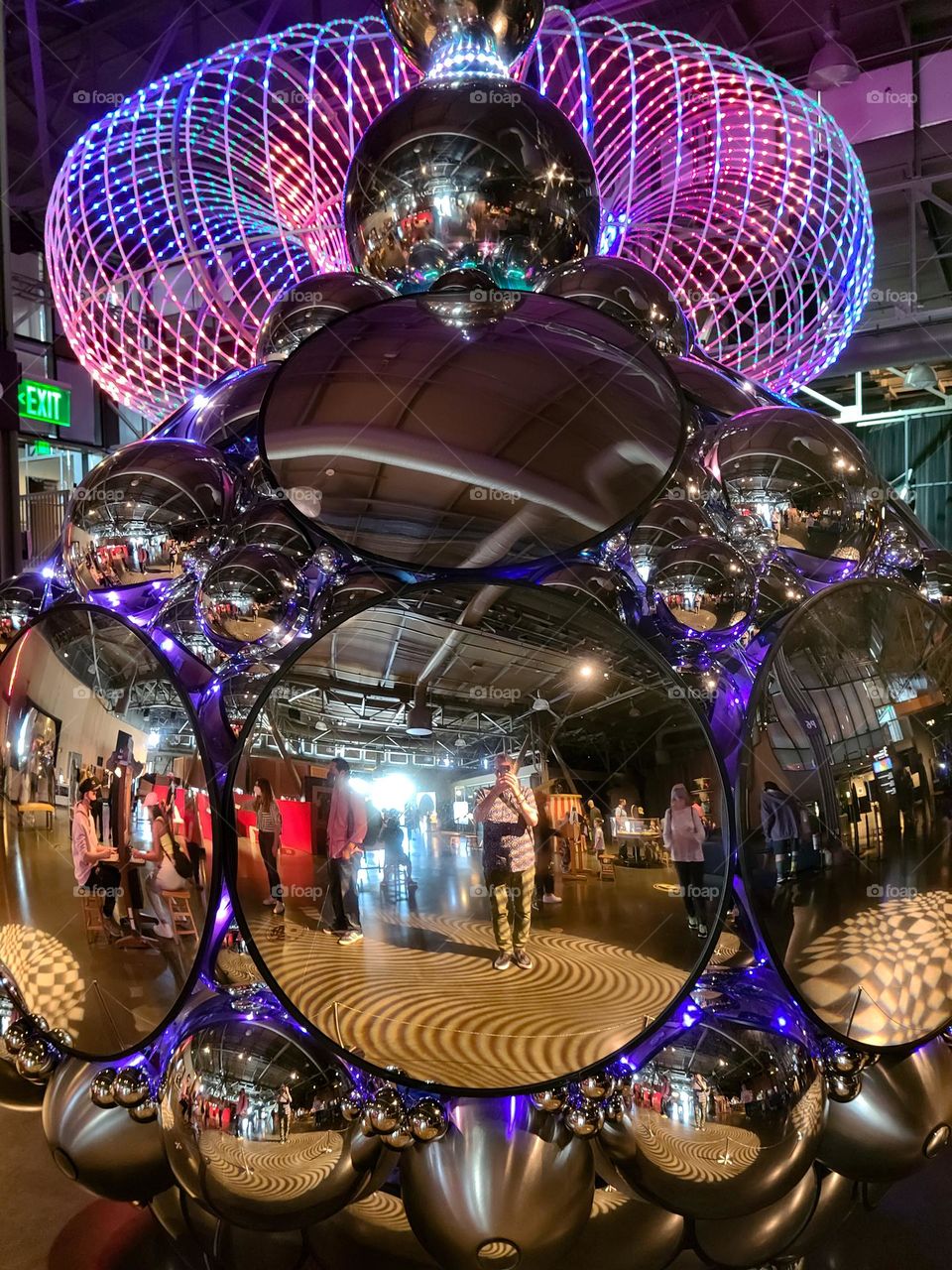 Mirror sculpture hanging from the ceiling, circular mirrors and vibrant neon colored lights create an experience for the eyes 