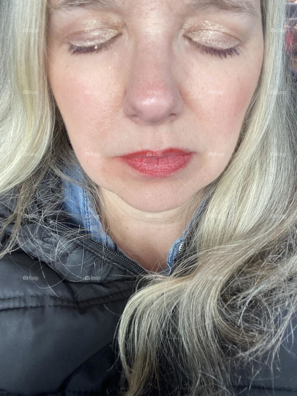 A selfie of me with my eyes closed to show my lids colored with a gold eyeshadow. I am wearing a Bare Minerals shade called “Queen Phyllis.” My lipstick is also Bare Minerals, Matte Liquid Lipcolor in “Fire.”