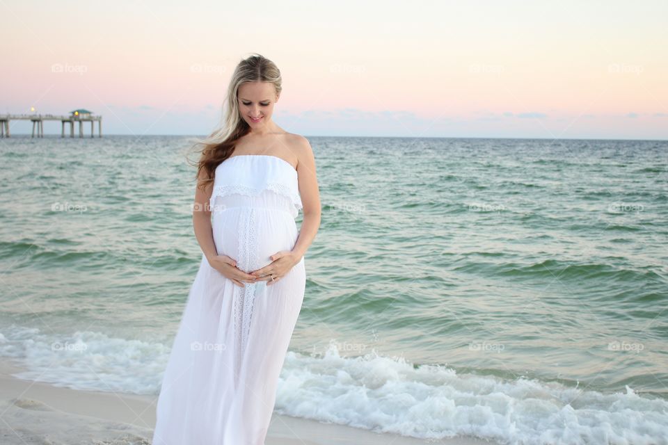 Pregnant woman in white dress standing near the coast