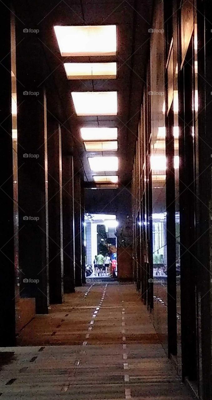 Shapes: rectangle. pedestrian corridor on the first floor of the building. all pillars, lights, walls, doors, floor are rectangles. a  family wanted to go home in distance at night. though corridor was dark, the family gave us warm feeling.