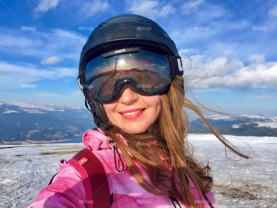 Portrait of pretty woman smiling wearing Uvex ski glasses and Uvex ski helmet surrounded by blue sky