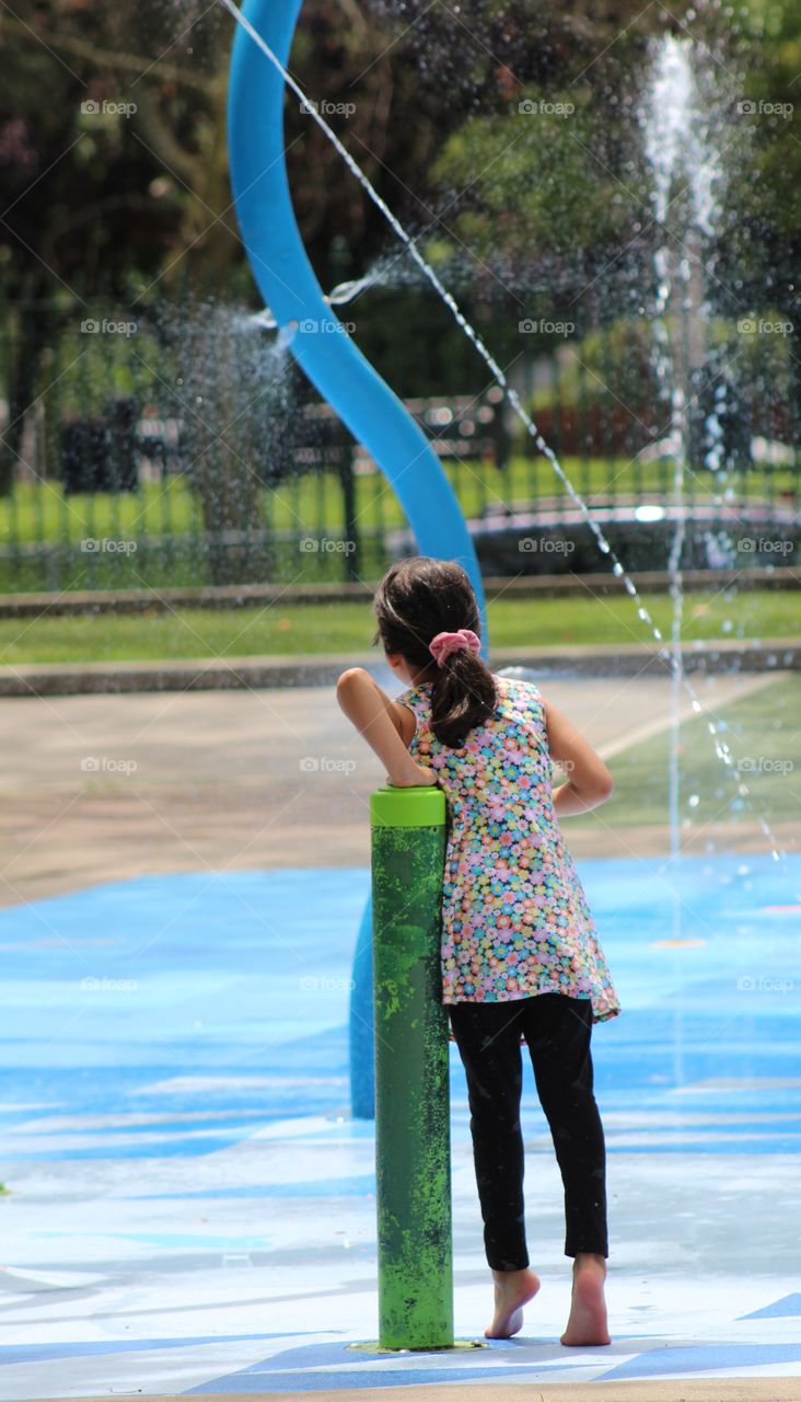 Little girl in waterpark standing on tiptoes to view water sprays in June 