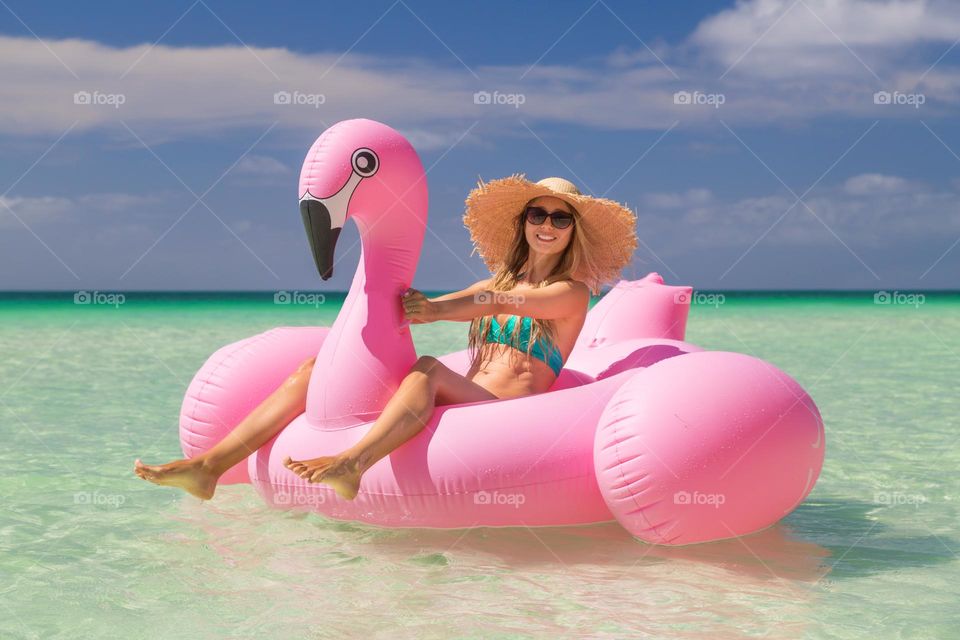 Happy Caucasian woman sitting in pink inflatable flamingo in sea
