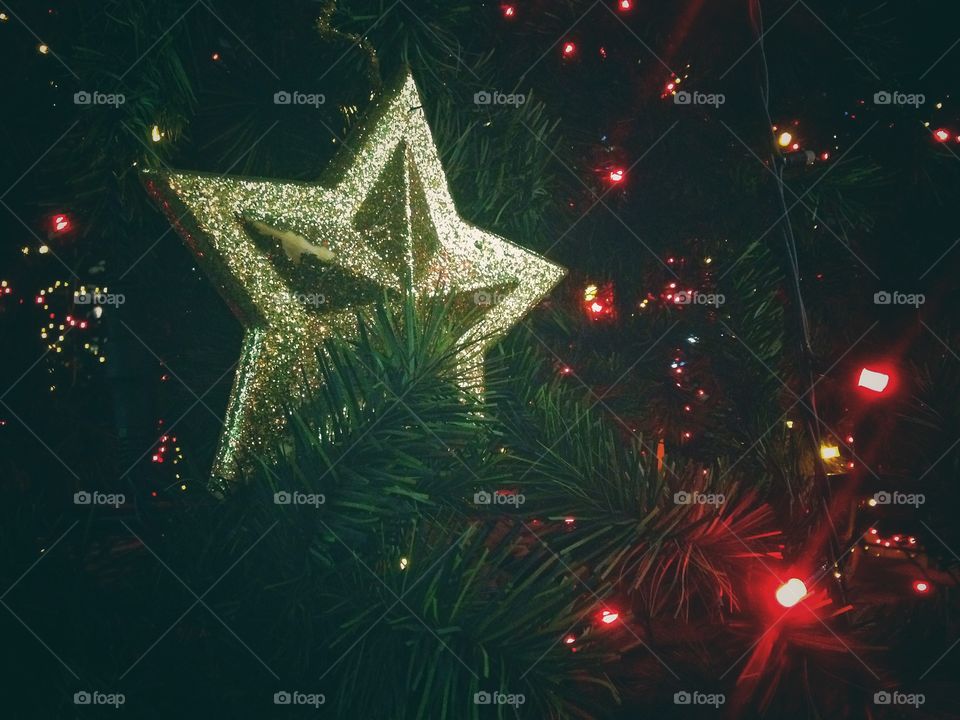 Gold plastic star, balls, red lights garland and other Christmas decorations on artificial fir tree in Moscow, Russia