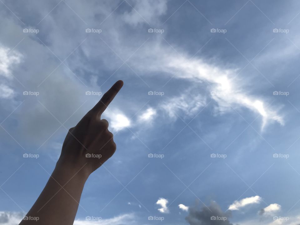 woman uses her right index finger pointing up in the bright blue sky with white cloud in daylight with copy space on the right side of frame