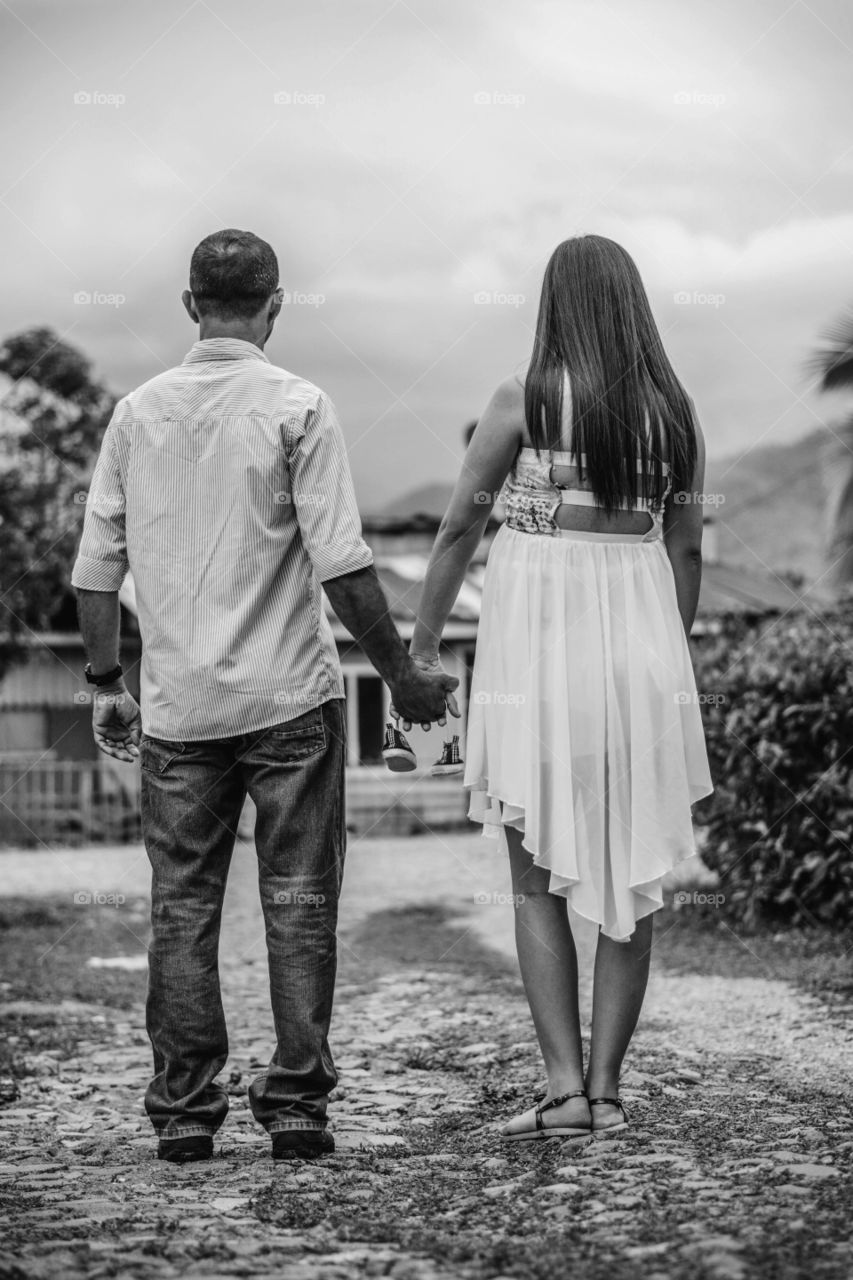 Pregnant couple holding hands with small shoes in their hands