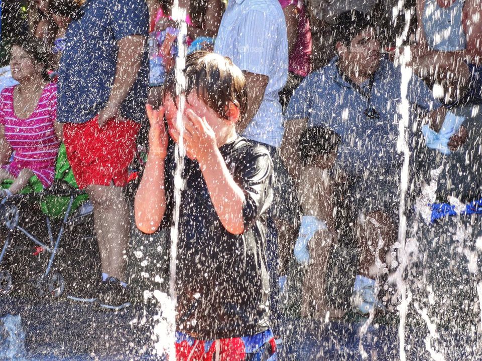 Boy Splashing In Water Fountain. Cooling Off In A Heat Wave
