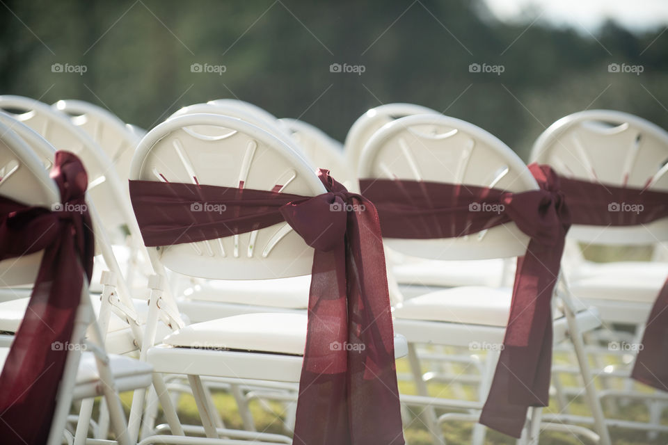 White wedding ceremony chairs with red bows and ribbons in rows