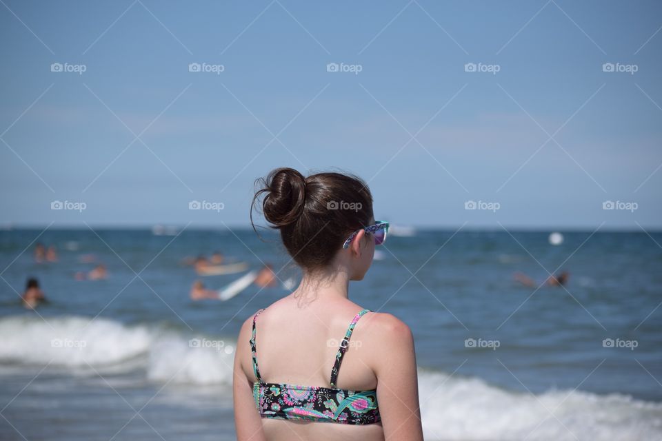 Watching the Surfers . A teen girl watching the surfers in the ocean.