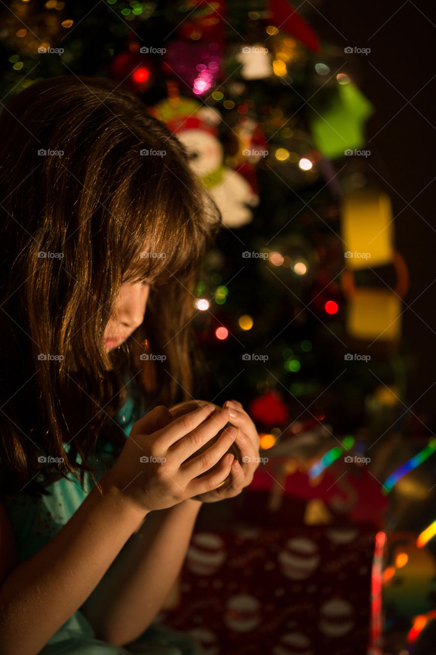 Christmas in our house a special time. Image of girl holding a ball with Christmas tree in the background
