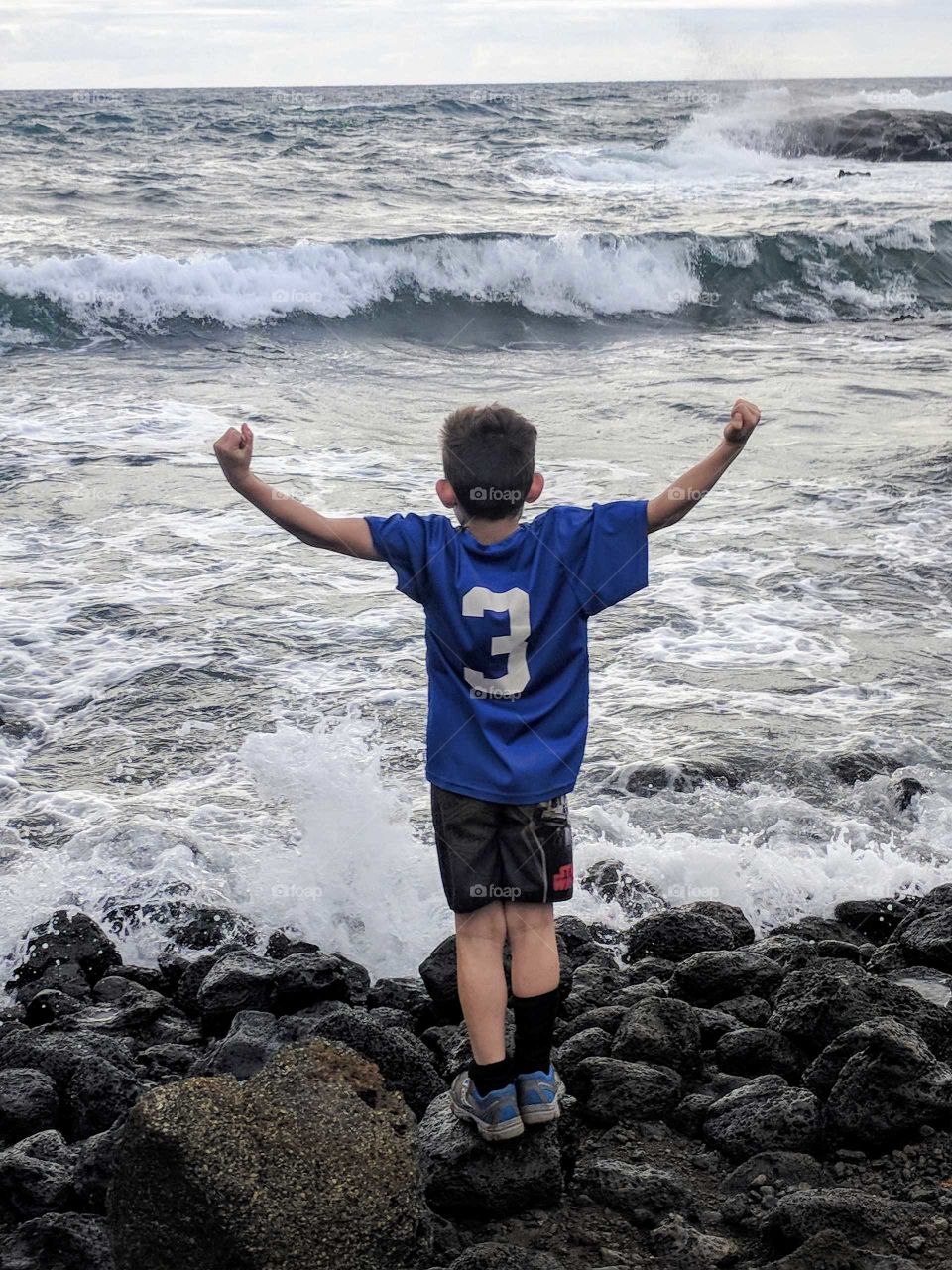 A boy flexes his muscles beside the ocean