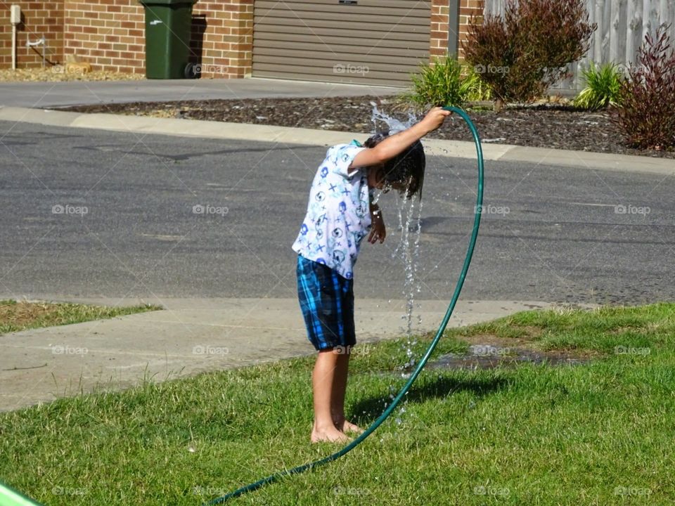 boy outside playing with the hose and squirting water over his head