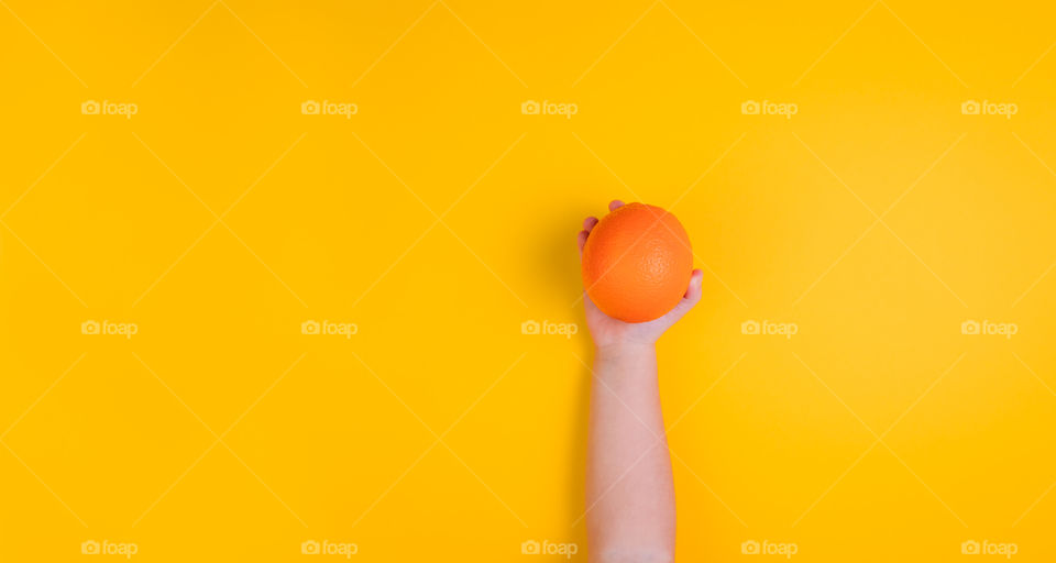 Little girl hand with orange fruit on orange background. Top view. Banner. Copy Space