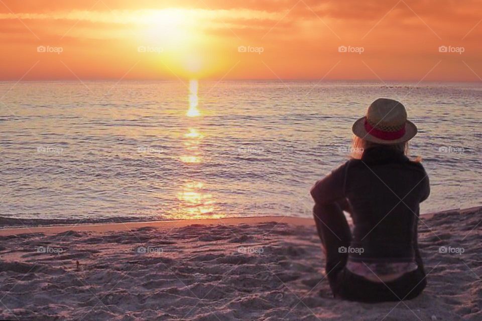 Woman on the beach watching the sun sink into the ocean.