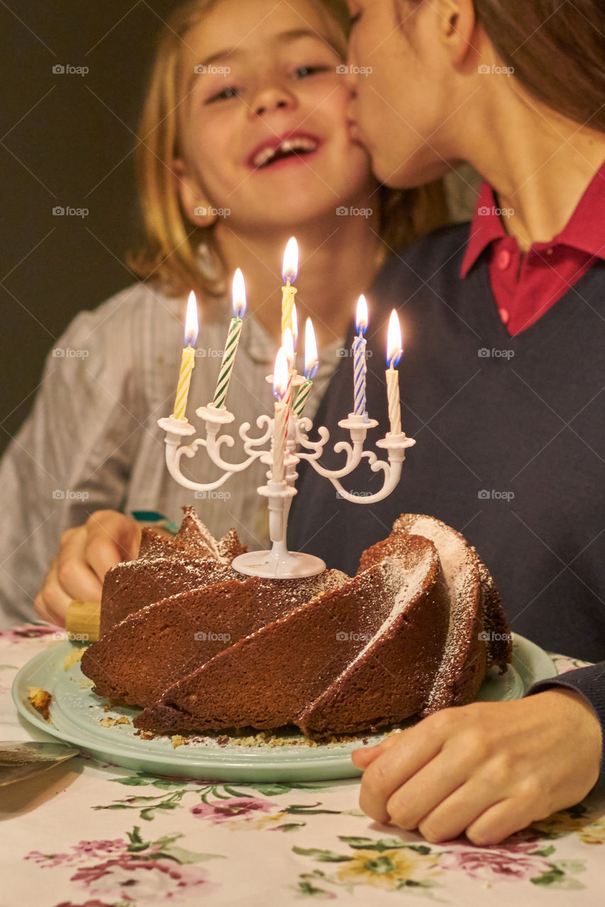 Person kissing girl on cheek with dessert on table