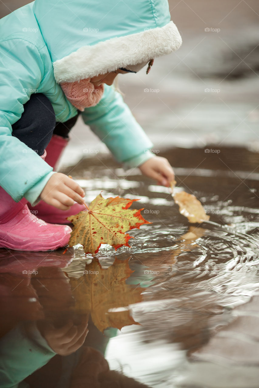 Little girl in rubber boots playing in puddle