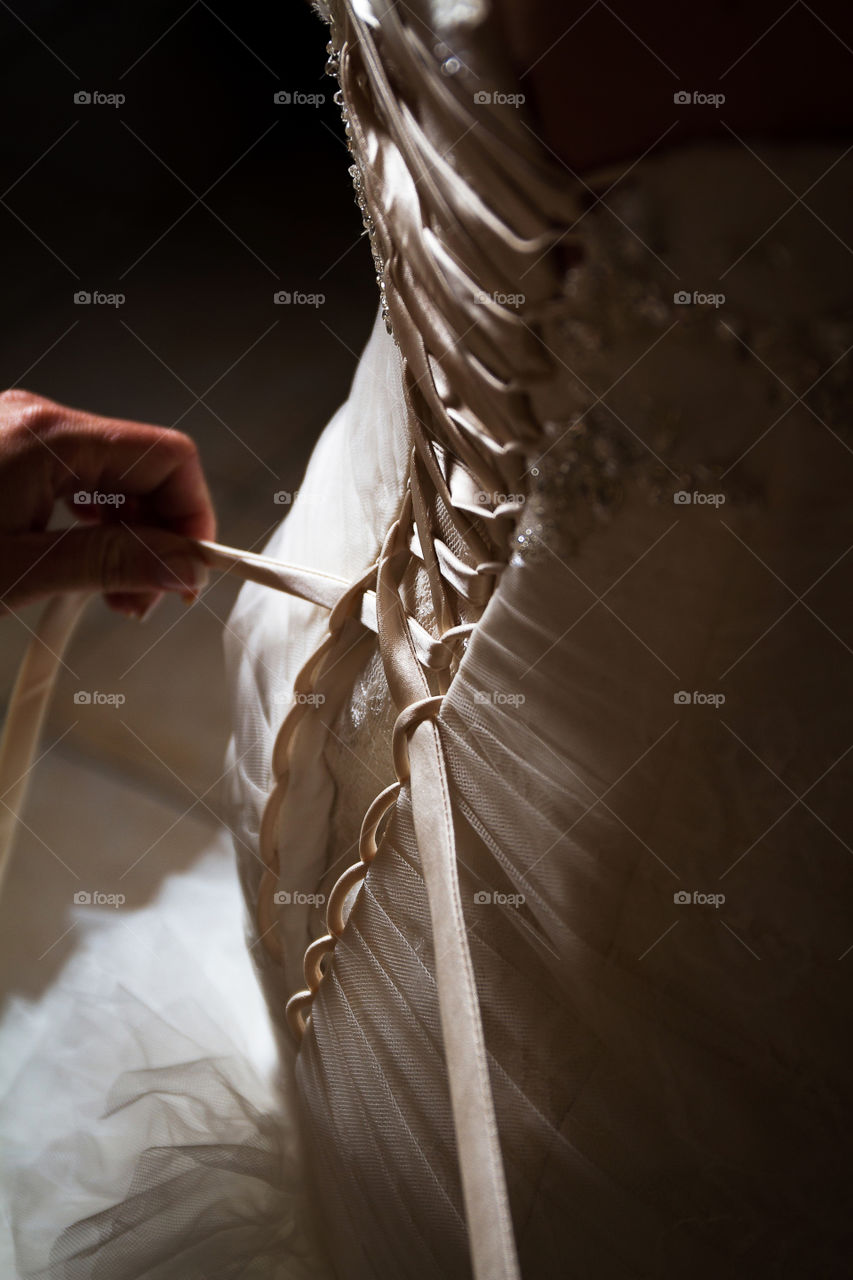Image of wedding dress being tied up. Love the shadows and light in this image showing the beautiful details of the dress.