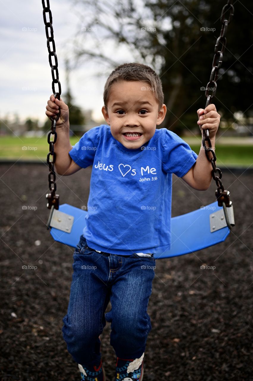 Close up shot of a boy smiling on the swing at the park 