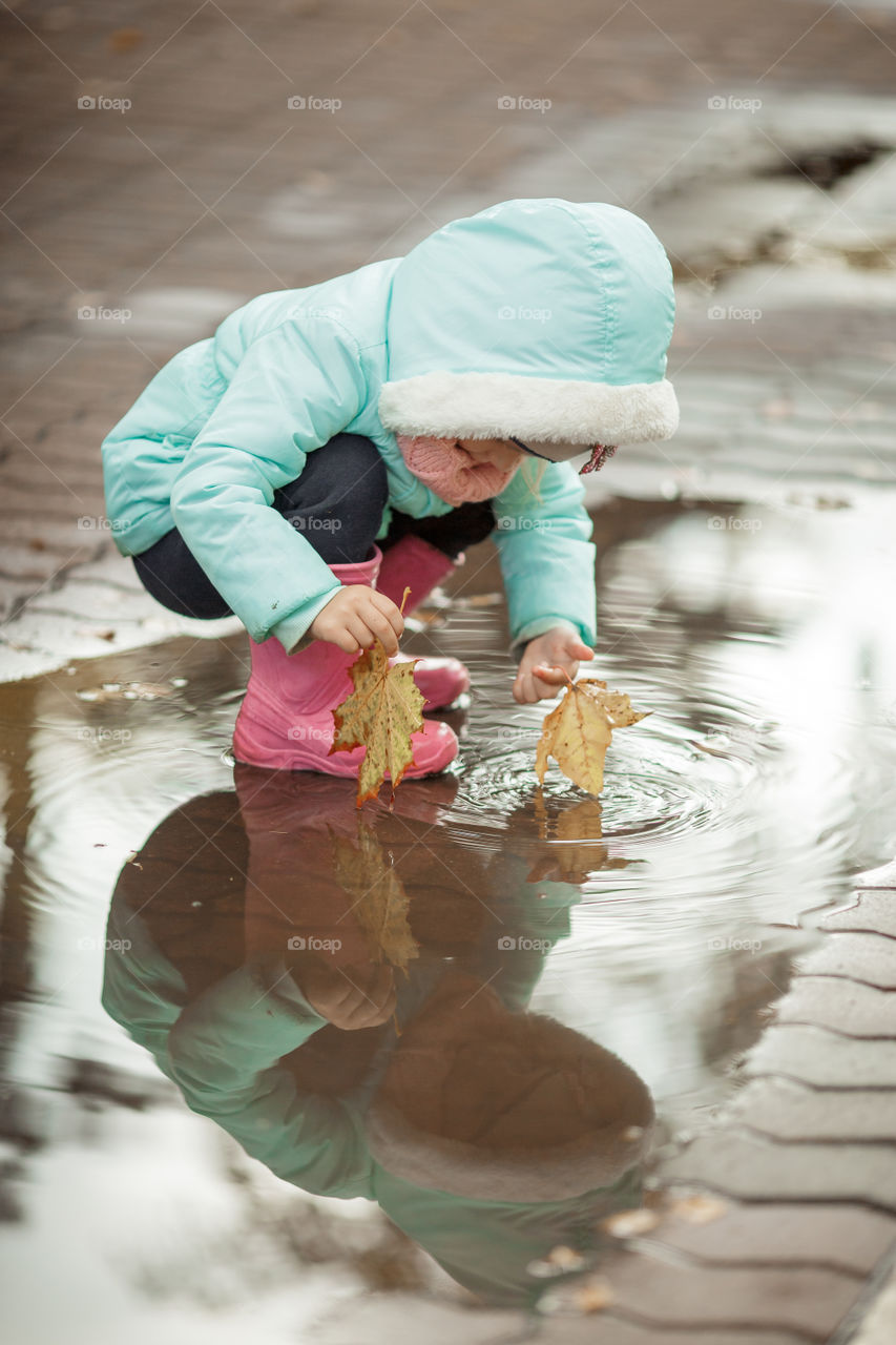 Little girl in rubber boots playing in puddle