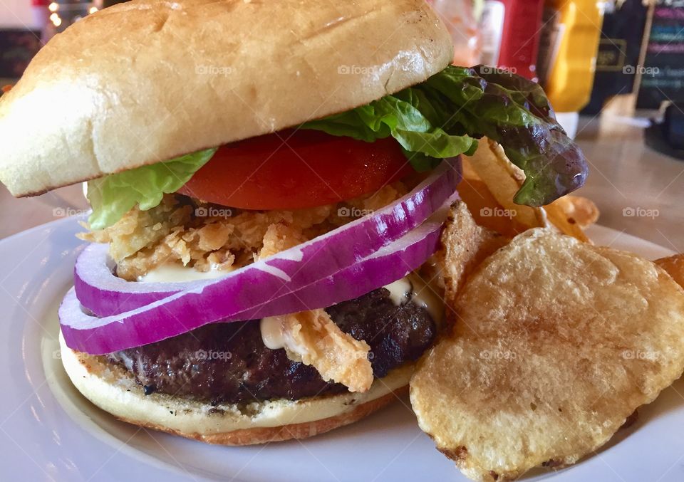 Delicious huge cheeseburger stacked high with lettuce tomato and onion on a plate with chips