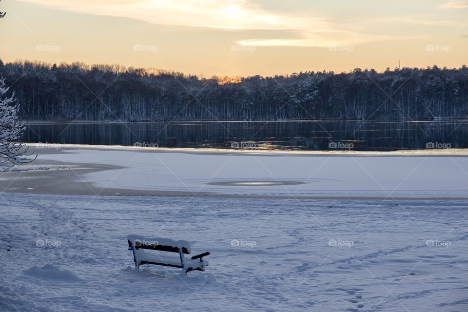 Winter wonderland, empty park bench by the lake at sunset - vinter och snö, en tom parkbänk i snöigt vinterlandskap med utsikt över sjö vid solnedgång 