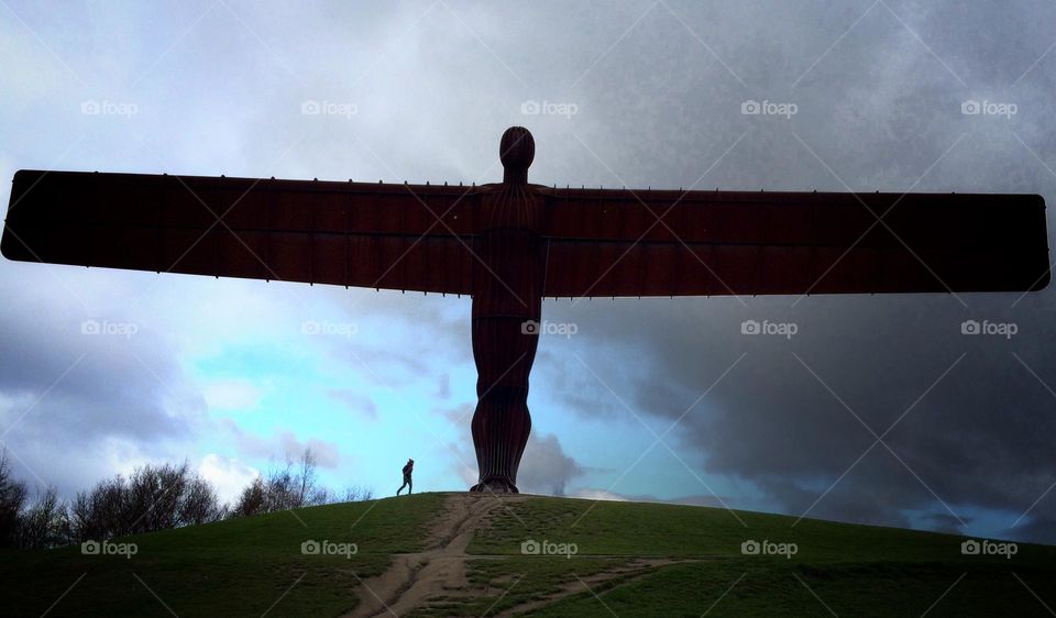 Minimalistic shot of The Angel of the North with one person passing underneath 