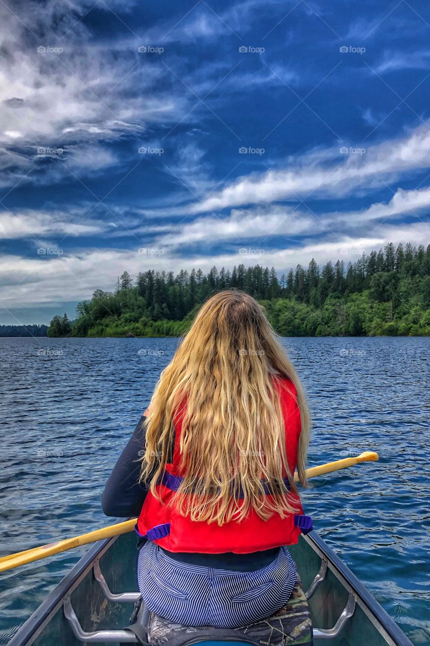 Long Blonde haired woman with vibrant colors paddling canoe in peaceful west coast BC Canada lake summer setting. 